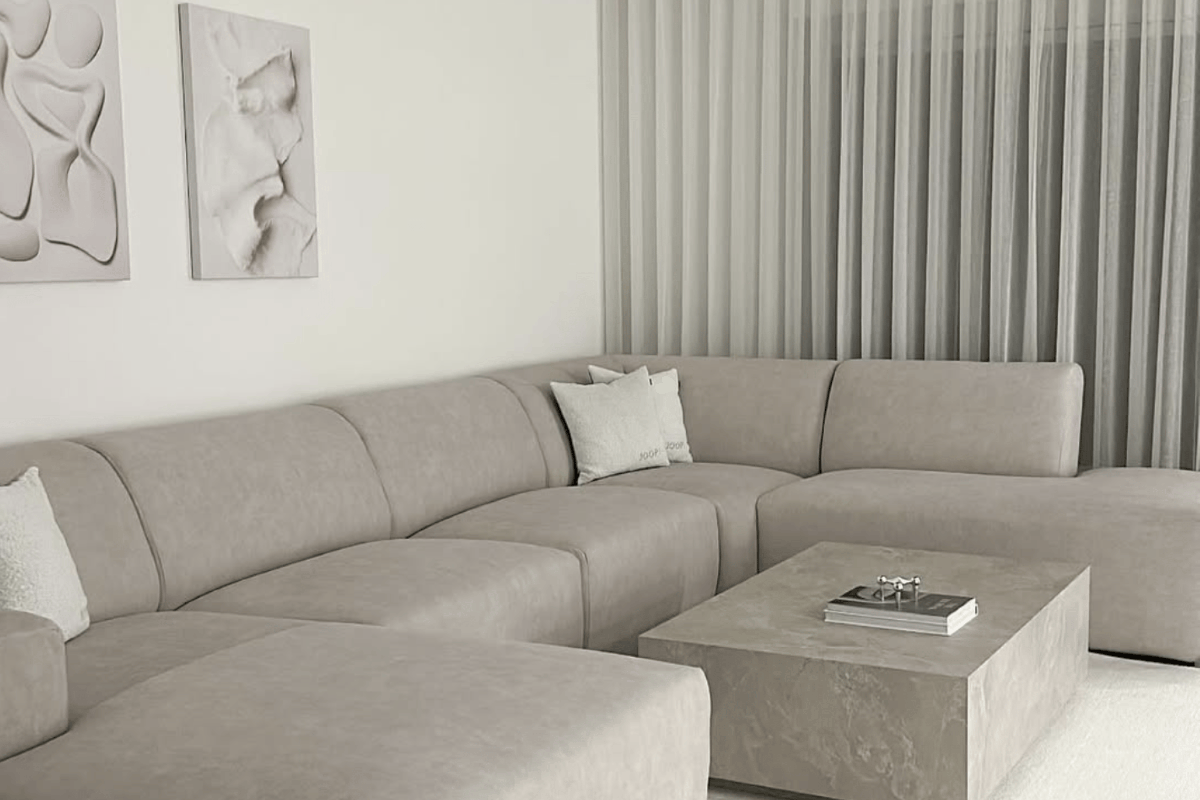 A neutral colored living room with off white walls, beige art and furniture including a couch, coffee table, and curtains.