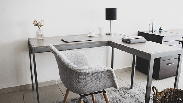 Gray chair in front of a simple gray desk with various office supplies on top and a small black lamp.