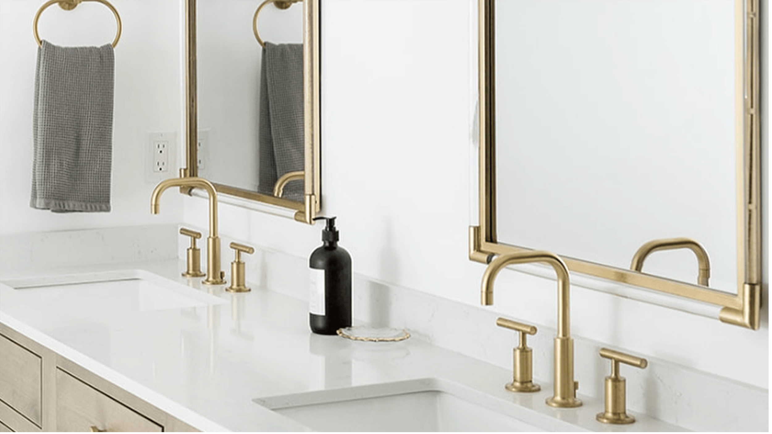 Two sinks and mirrors in a bathroom with white counter tops and gold hardware.