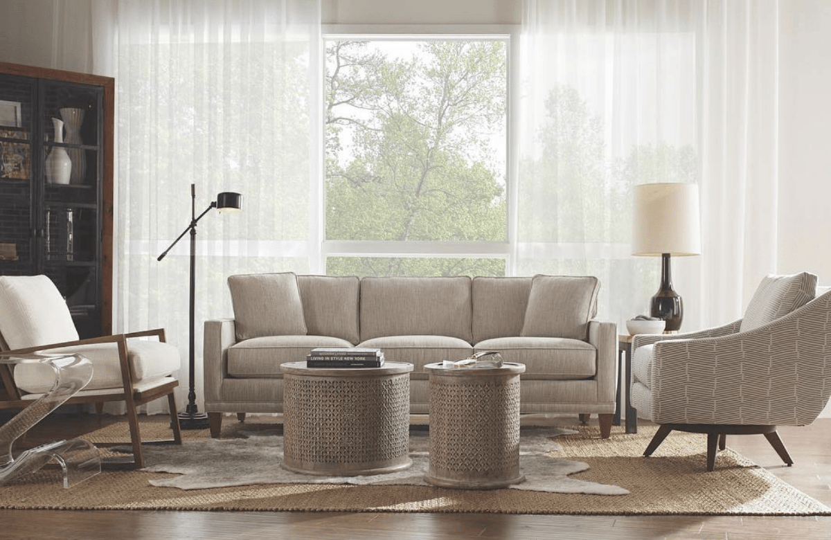 A living room with a lot of natural light, a brown rug, and beige couch, chairs, and center tables.