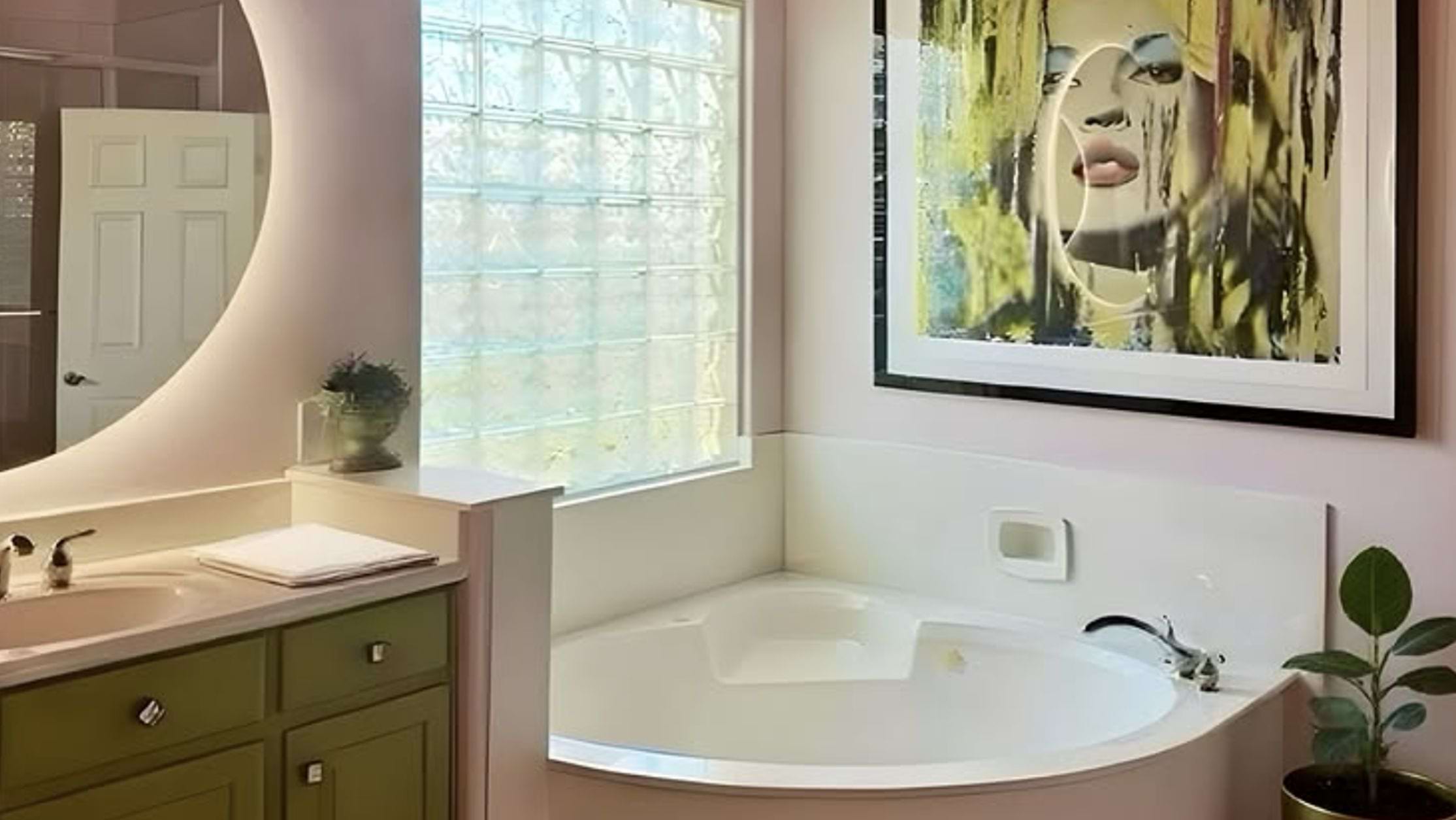 A light pink bathroom with ceramic features and a statement art print above the large tub.
