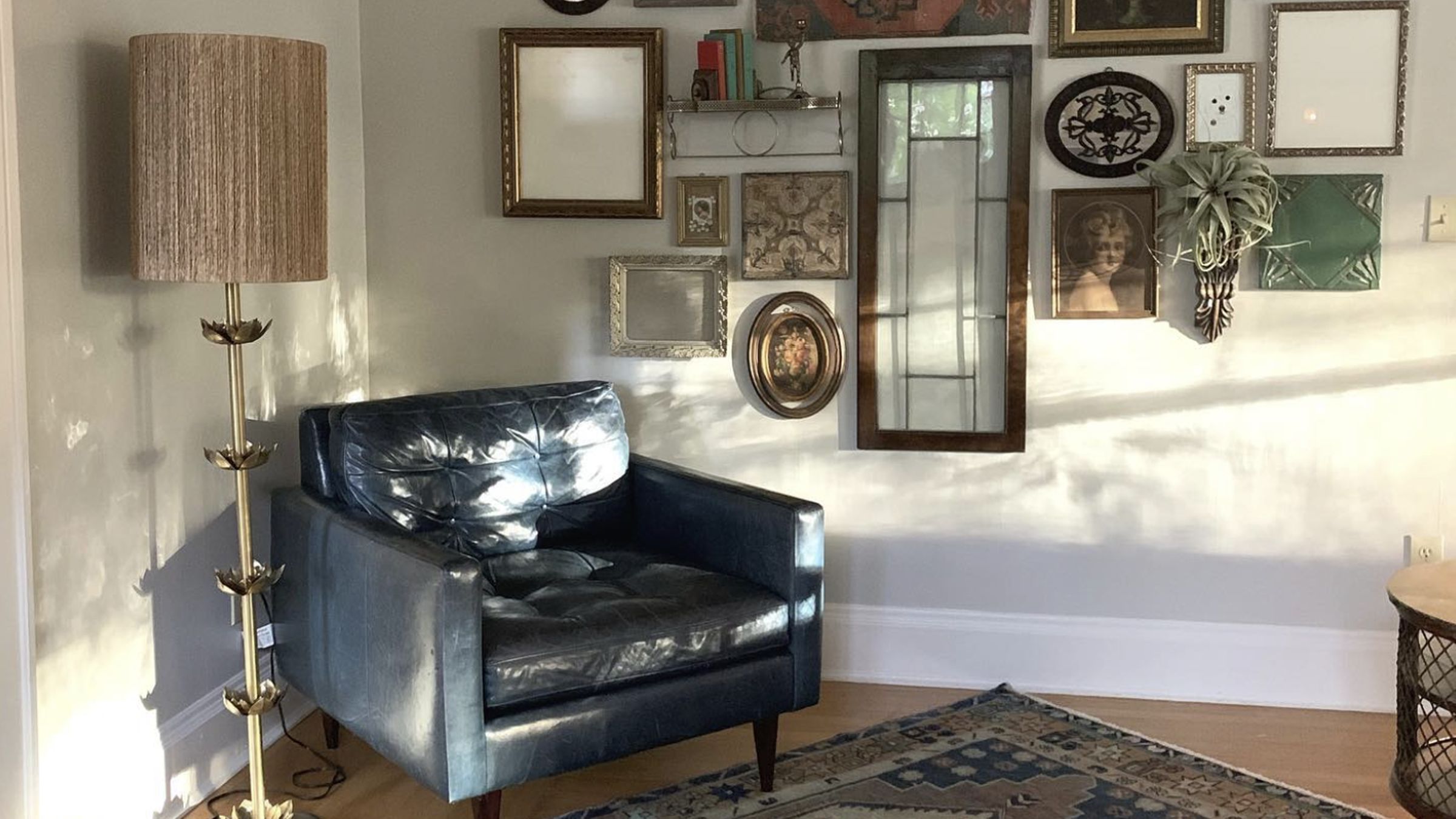 Small room with natural sunlight, a leather chair sits in front of a gallery wall displaying many framed photos, mirrors, and hanging plants.