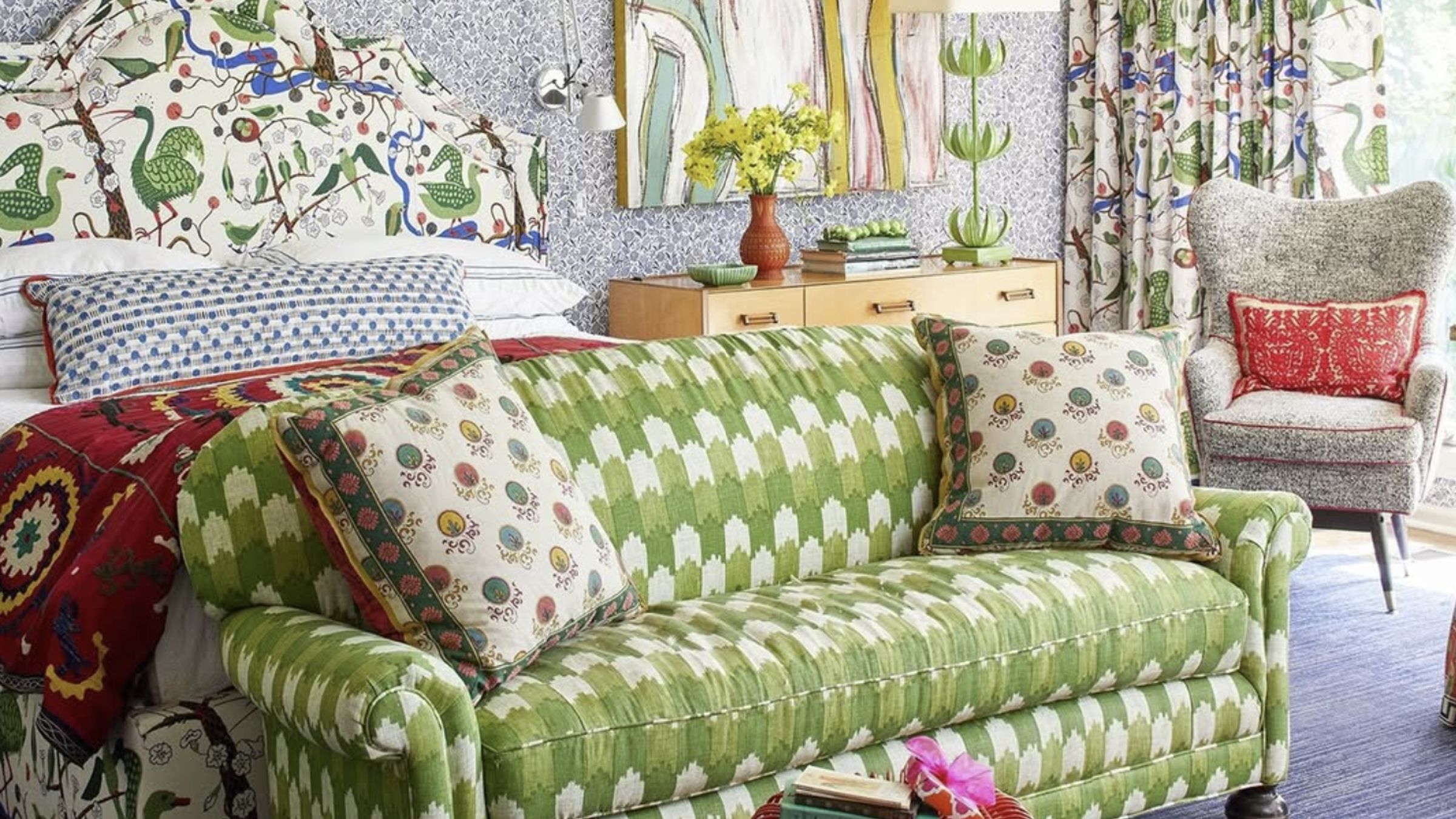 A bedroom with a bed, couch, chair and curtains, all featuring busy pattern. This is an example of a room with a maximalist design aesthetic.