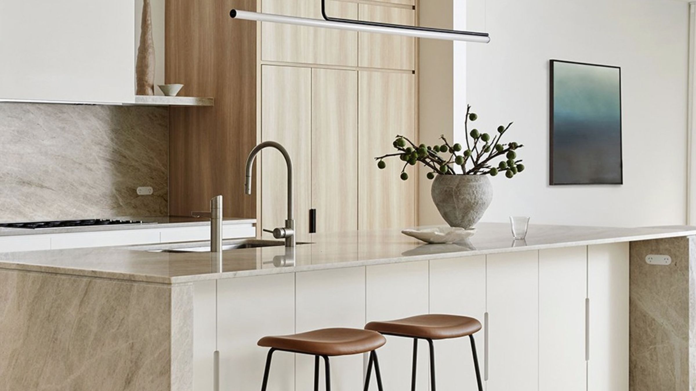 A sleek and modern kitchen with only a few simple items accessorizing the walls and counter including a plant and a few stools.