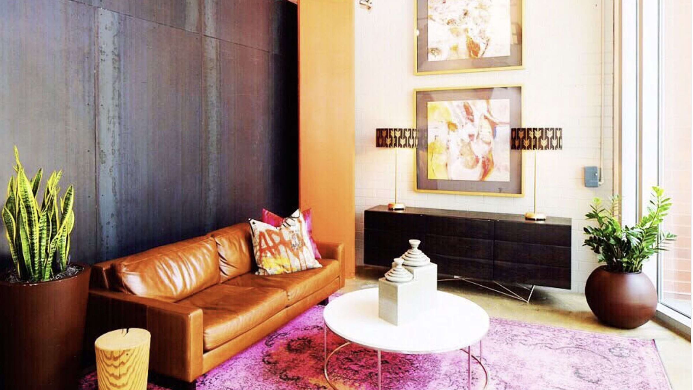 A sitting room with a bright fusia rug, and more neutral brown couch and black credenza.