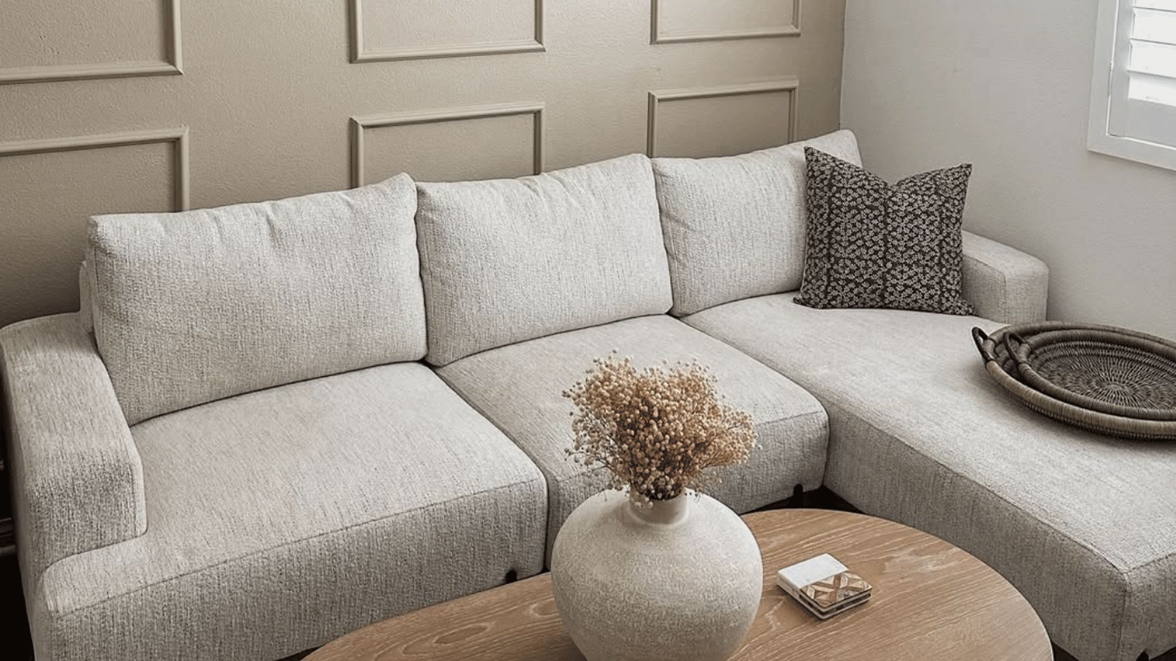 Small living room with a couch, coffee table, and vase all in differing tones of beige.