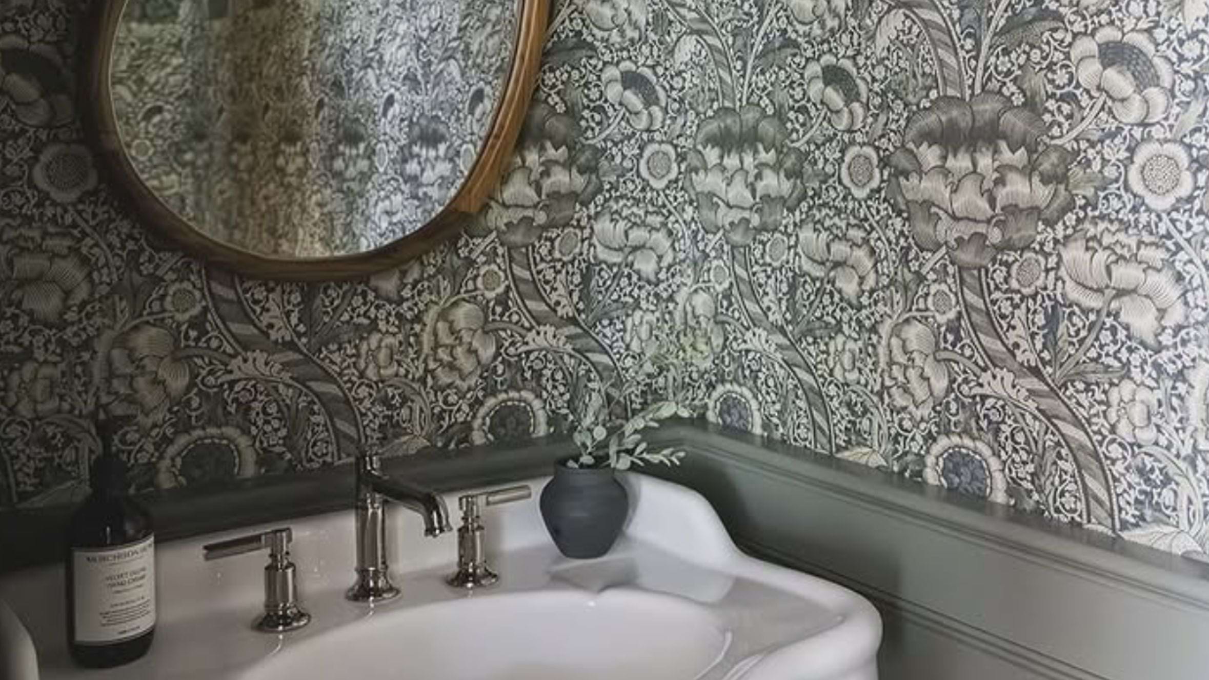A small powder room bathroom with bold gray and white wall paper and coordinating accessories around the sink.