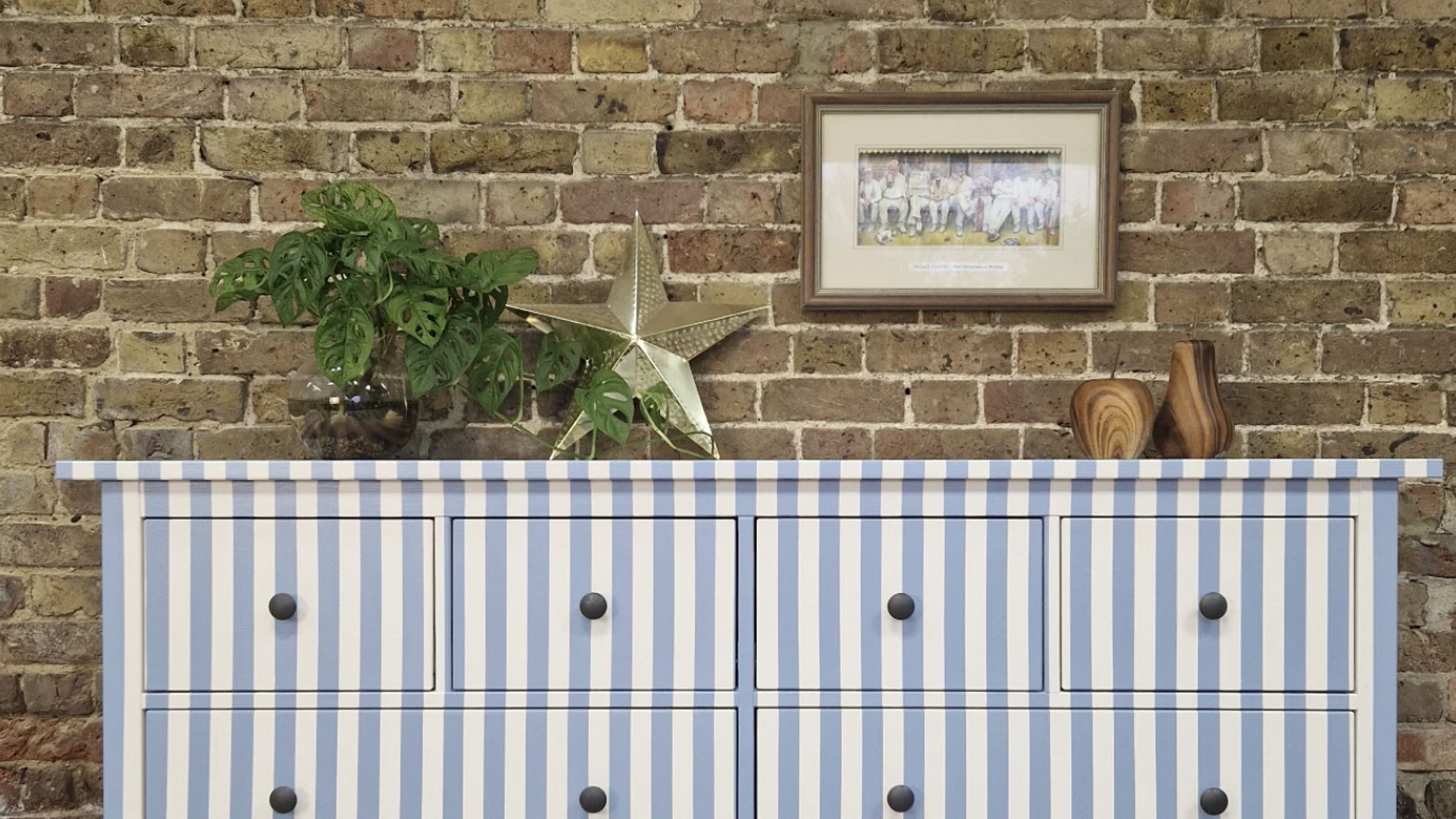 A dresser with blue and white vertical stripes sits in front of a brick wall.
